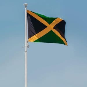 The Jamaican flag waving on a white flagpole against a clear blue sky.