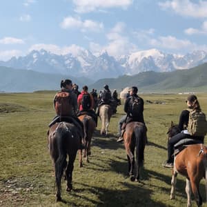 Eine WeRoad Gruppenreise zu Pferd über eine Graslandschaft auf schneebedeckte Berge zu.