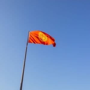 Die rot-gelbe Flagge Kirgisistans weht an einem hohen Fahnenmast vor einem klaren blauen Himmel.