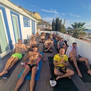 Un gruppo WeRoad è seduto su tappetini da yoga su una terrazza soleggiata sul tetto, in posa per una foto dopo una sessione di yoga.