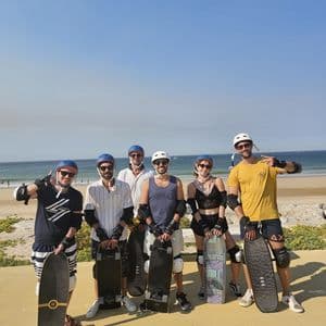 Un gruppo WeRoad in viaggio, con i caschi, posa con gli skateboard su un lungomare vicino a una spiaggia soleggiata.