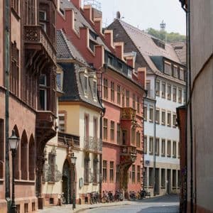 Una stretta strada acciottolata, fiancheggiata da edifici storici e colorati, con biciclette parcheggiate in una giornata di sole.