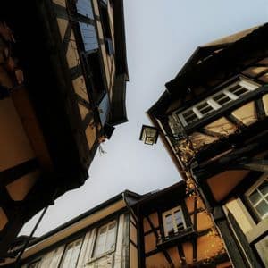Una vista dal basso di tradizionali edifici a graticcio che fiancheggiano una strada stretta sotto un cielo pallido.