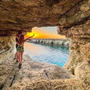 Una coppia si abbraccia all'interno di una grotta marina rocciosa, guardando il tramonto su un mare calmo.