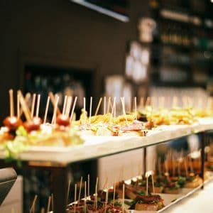 A variety of tapas with toothpicks arranged on long platters on a bar counter in a dimly lit restaurant.