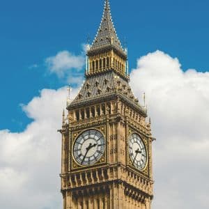 A low-angle shot of the Big Ben clock tower against a blue sky with white clouds.