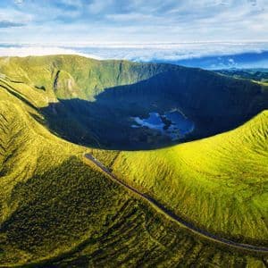 Una vista aerea di un grande cratere vulcanico verde con un lago sul fondo e una strada che si snoda lungo il suo bordo.
