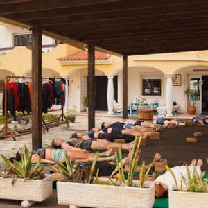 Un viaggio di gruppo WeRoad pratica yoga, sdraiato in posa di rilassamento su tappetini su una piattaforma esterna coperta.