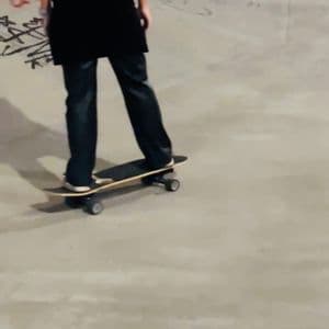 Una donna dai lunghi capelli scuri, vista di spalle, che fa skateboard in uno skatepark di cemento.