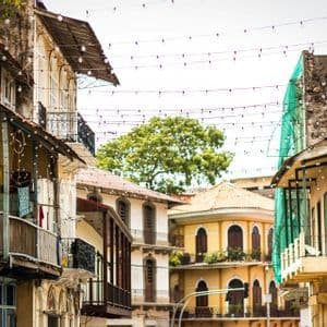 A narrow street is lined with colorful colonial-style buildings featuring balconies and strings of lights crisscrossing overhead.