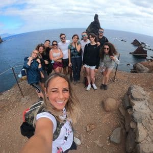 Une femme prend un selfie avec un voyage de groupe WeRoad sur une falaise surplombant un littoral rocheux et l'océan.