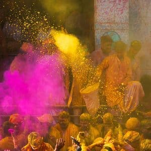 Una folla di persone a un festival lancia polvere gialla e rosa vibrante in aria.