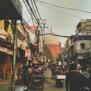 Una vivace scena di strada con persone, risciò e cavi aerei aggrovigliati, con una grande moschea a cupola visibile alla fine della strada.