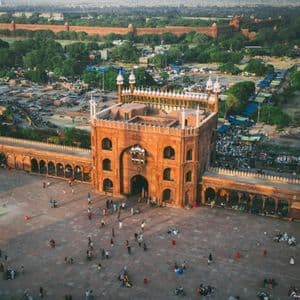 Veduta aerea di una moschea di arenaria rossa con persone nel suo ampio cortile, con una città e mura di un forte sullo sfondo.