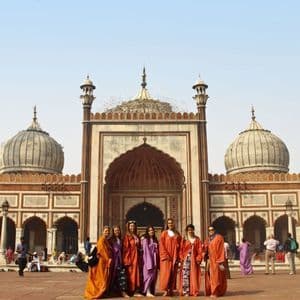 Un grupo de mujeres WeRoad, vistiendo túnicas coloridas, posa para una foto frente a una mezquita ornamentada con grandes cúpulas.