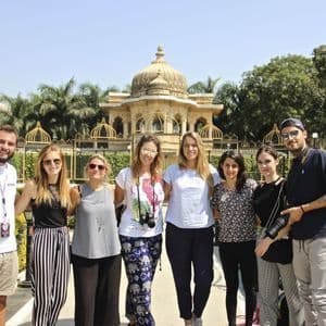 Un grupo de WeRoad de viaje sonríe para una foto en un jardín cuidado frente a un edificio ornamentado con cúpulas doradas.