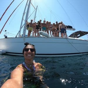 Eine lächelnde Frau macht ein Selfie aus dem Wasser, während eine WeRoad-Gruppenreise an Deck eines Segelbootes posiert.