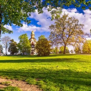 Un bâtiment historique avec un dôme sur une colline herbeuse, entouré d'arbres verts sous un ciel partiellement nuageux.
