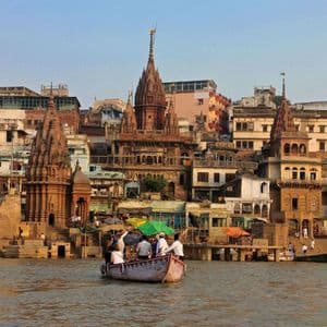 Un viaggio di gruppo WeRoad in barca su un fiume, passando per templi storici e edifici sul lungofiume sotto un cielo sereno.