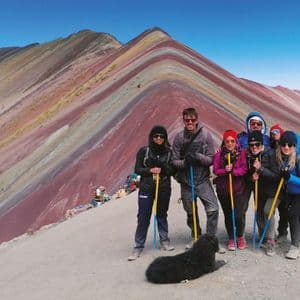 Eine WeRoad-Gruppenreise mit einem schwarzen Hund, der auf einem Bergkamm posiert, vor dem Hintergrund bunter, gestreifter Berge.