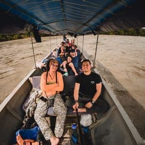 Weitwinkel-Selfie einer WeRoad-Gruppenreise in einem überdachten Langboot auf einem schlammigen Fluss.