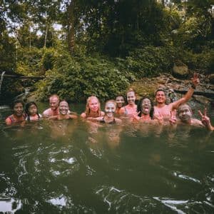 Eine WeRoad Gruppe lächelt mit Schlammmasken im Gesicht, während sie in einem Naturpool im Dschungel badet.