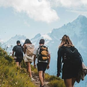 Un gruppo WeRoad visto da dietro, in escursione su uno stretto sentiero di montagna erboso con cime rocciose sullo sfondo.