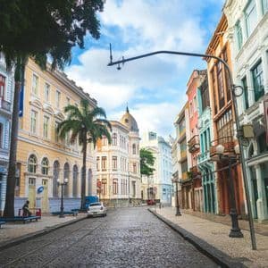 Uno scorcio di una strada acciottolata con binari del tram, fiancheggiata da edifici colorati di epoca coloniale e palme.