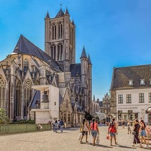 La gente camina por una plaza soleada con una gran catedral gótica y edificios históricos al fondo.