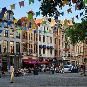 Una soleada plaza adoquinada en una ciudad europea, con gente en los cafés y coloridas guirnaldas de banderas colgando.