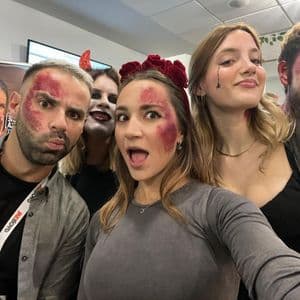 Un gruppo di persone con trucco in stile Halloween e glitter rosso posa insieme per un selfie, facendo facce giocose.