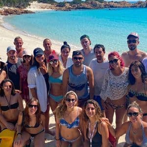 Un viaggio di gruppo WeRoad in posa per una foto su una spiaggia di sabbia bianca con acqua turchese cristallina sullo sfondo.