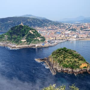 Una vista aerea di due isole verdi e lussureggianti in una baia blu profonda, con una città costiera e dolci colline sullo sfondo.