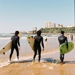 Un viaggio di gruppo WeRoad: tre surfisti in muta che trasportano le tavole da surf mentre entrano in mare dalla spiaggia.