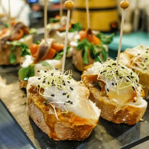 Un primo piano di vari pintxos spagnoli con pesce e germogli su un piatto da portata scuro, ognuno fissato con uno stuzzicadenti.