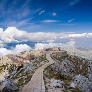 Un sentiero in pietra tortuoso porta a un belvedere circolare su una vetta di montagna, dove un gruppo WeRoad si gode la vista panoramica.