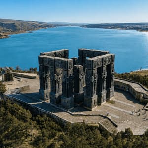 Veduta aerea di un grande monumento in pietra scura, situato su una piazza collinare, con vista su un vasto lago blu sotto un cielo limpido.