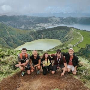 A WeRoad group trip of five people crouching on a viewpoint overlooking a valley with two volcanic crater lakes and lush green hills.