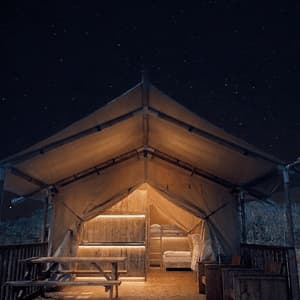 Una grande tenda glamping illuminata con un ponte in legno e un tavolo da picnic sotto un cielo stellato.