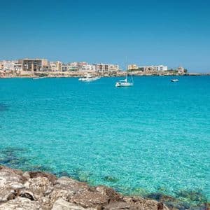 Una costa rocciosa si affaccia su una baia turchese con diverse barche ancorate vicino a una località costiera.