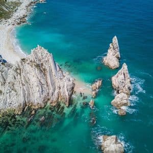Una vista aerea di alte formazioni rocciose bianche e scogliere lungo una costa con acqua turchese e blu intenso.
