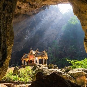 Un pavillon thaïlandais doré se dresse à l'intérieur d'une grande grotte, éclairé par un seul rayon de soleil provenant d'une ouverture au plafond.