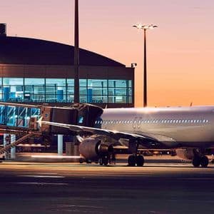 Un aereo è parcheggiato al gate di un terminal aeroportuale, collegato da un finger durante un tramonto colorato.