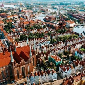 Una veduta aerea in tilt-shift di una città storica con tetti in tegole rosse, una grande cattedrale e un fiume che serpeggia al suo interno.