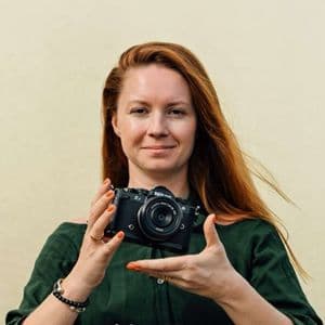 Eine Frau mit langen roten Haaren und einem grünen Oberteil hält eine schwarze Nikon Z spiegellose Kamera mit beiden Händen hoch.