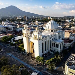 Veduta aerea di una grande cattedrale bianca con cupola, al centro di una città e un vulcano sullo sfondo.