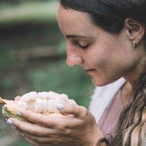 Una donna di profilo, con gli occhi chiusi, che annusa la polpa bianca di un baccello di cacao appena aperto.