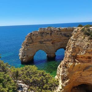 Una grande formazione rocciosa costiera presenta due archi naturali su acque turchesi in una giornata di sole.