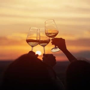 Sagome di un gruppo WeRoad che brinda con tre calici di vino bianco al tramonto arancione.