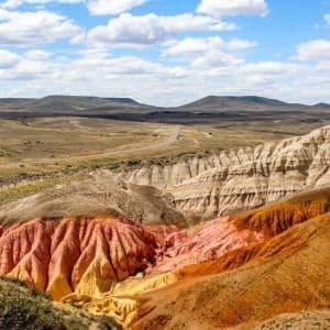 Un canyon con formazioni rocciose rosse, arancioni e gialle in un paesaggio arido sotto un cielo parzialmente nuvoloso.